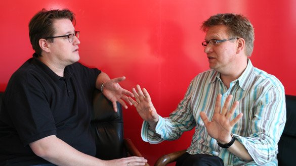 Claudius Grigat und Frank Muchlinsky im Gespräch vor rotem Hintergrund